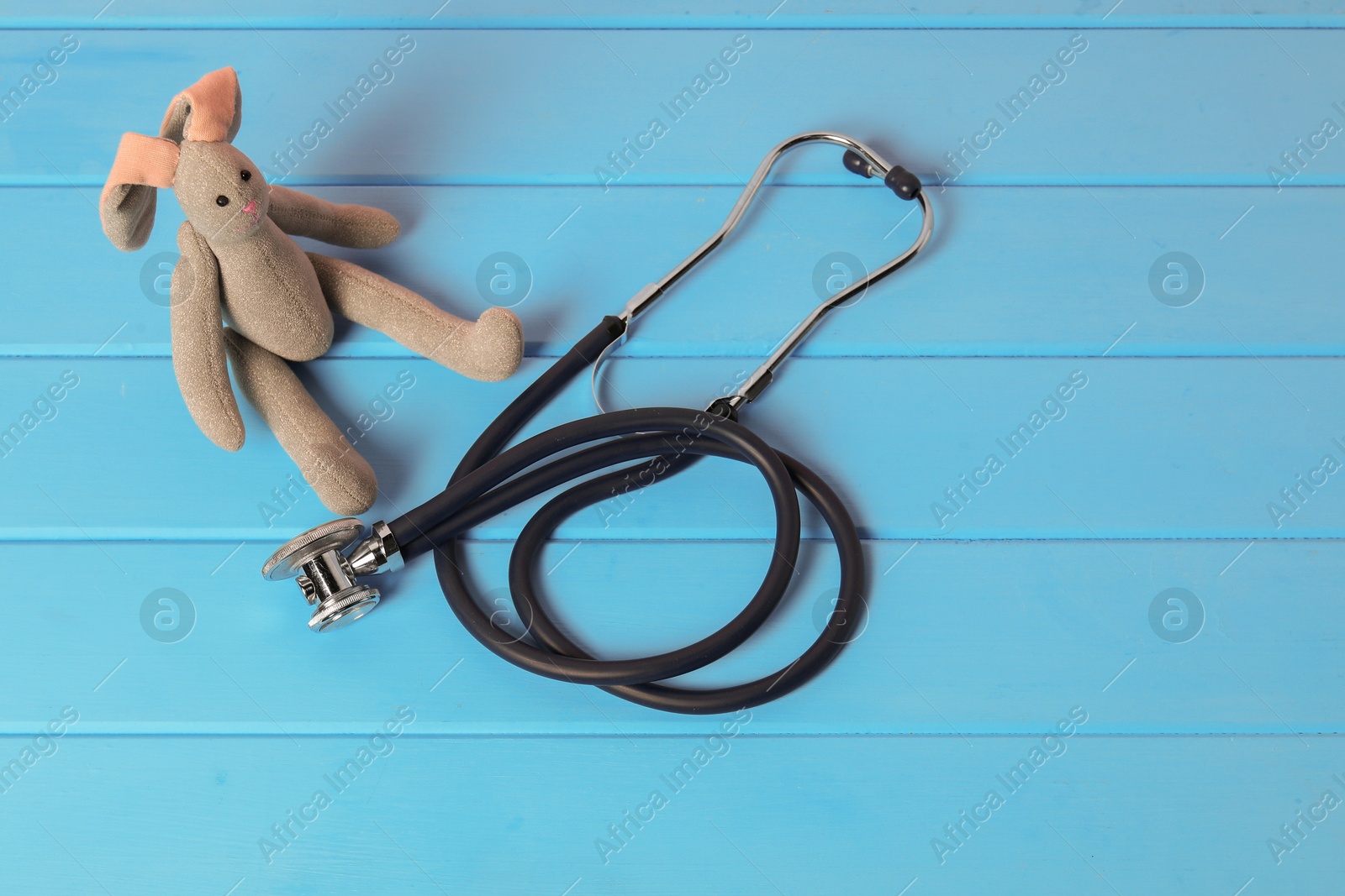 Photo of Pediatrics concept. Toy bunny and stethoscope on light blue wooden table, above view. Space for text