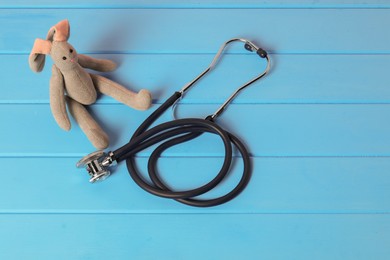 Photo of Pediatrics concept. Toy bunny and stethoscope on light blue wooden table, above view. Space for text