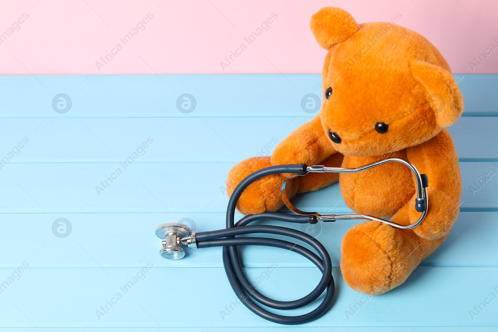 Photo of Pediatrics concept. Teddy bear and stethoscope on light blue wooden table, space for text