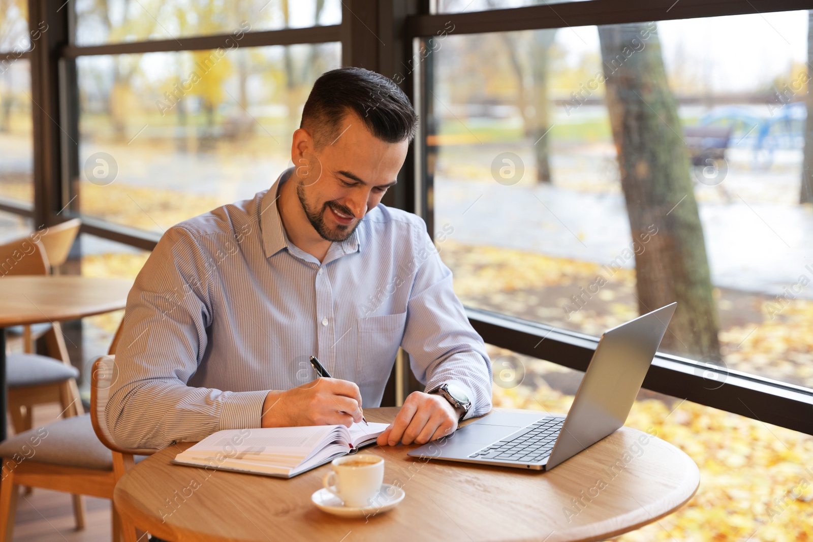 Photo of Man taking notes at table in cafe