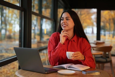 Photo of Woman with cup of coffee working at table in cafe