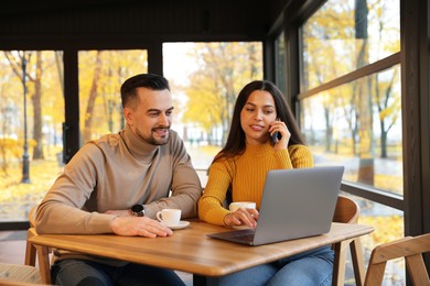 Photo of Colleagues with laptop working together at table in cafe