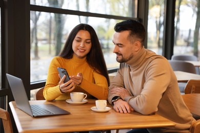 Photo of Woman showing something on smartphone to man at table in cafe