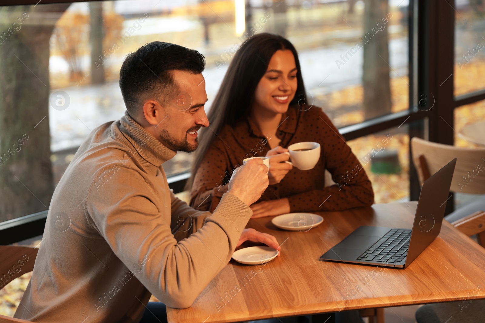 Photo of Colleagues with cups of coffee and laptop working together at table in cafe