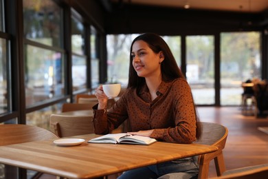 Photo of Woman with cup of coffee working at table in cafe