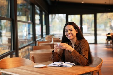 Photo of Woman with cup of coffee working at table in cafe