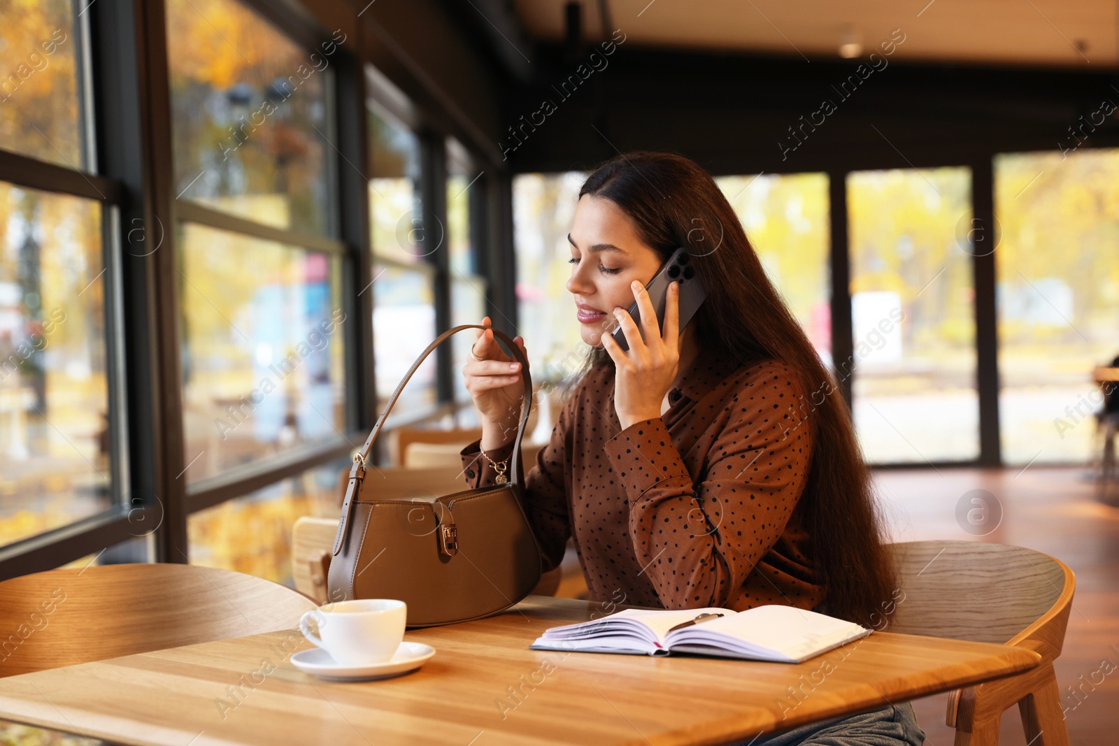 Photo of Woman with bag talking on smartphone at table in cafe