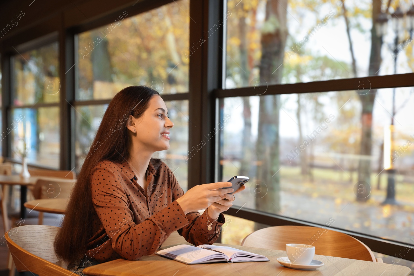 Photo of Woman using smartphone while working at table in cafe