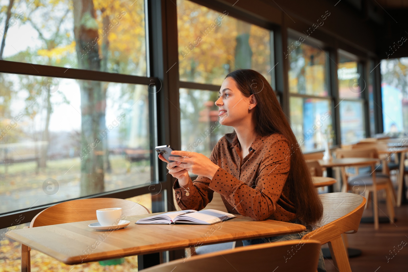 Photo of Woman using smartphone while working at table in cafe