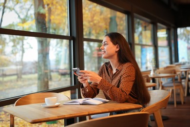 Photo of Woman using smartphone while working at table in cafe