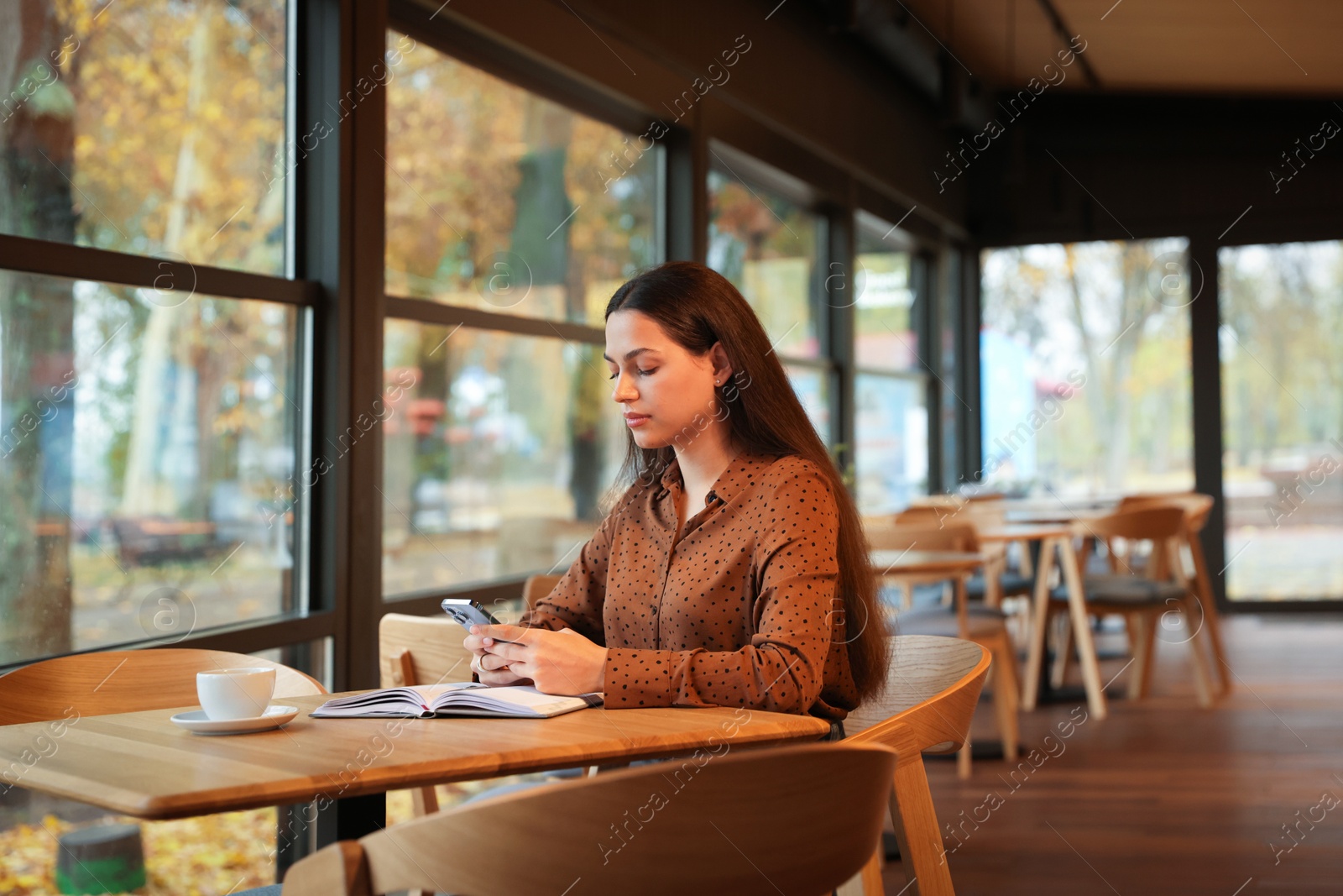 Photo of Woman using smartphone while working at table in cafe