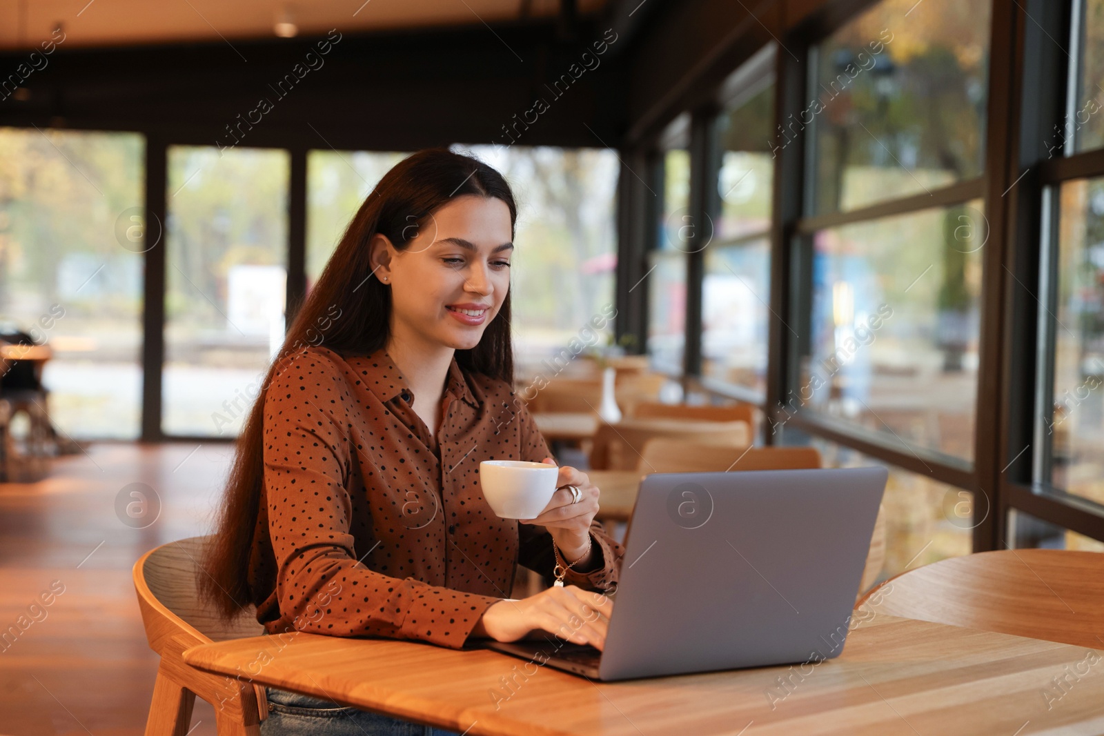 Photo of Woman with cup of coffee working on laptop at table in cafe