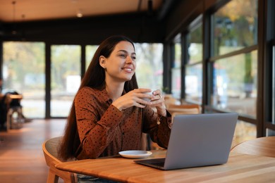 Photo of Woman with cup of coffee working at table in cafe