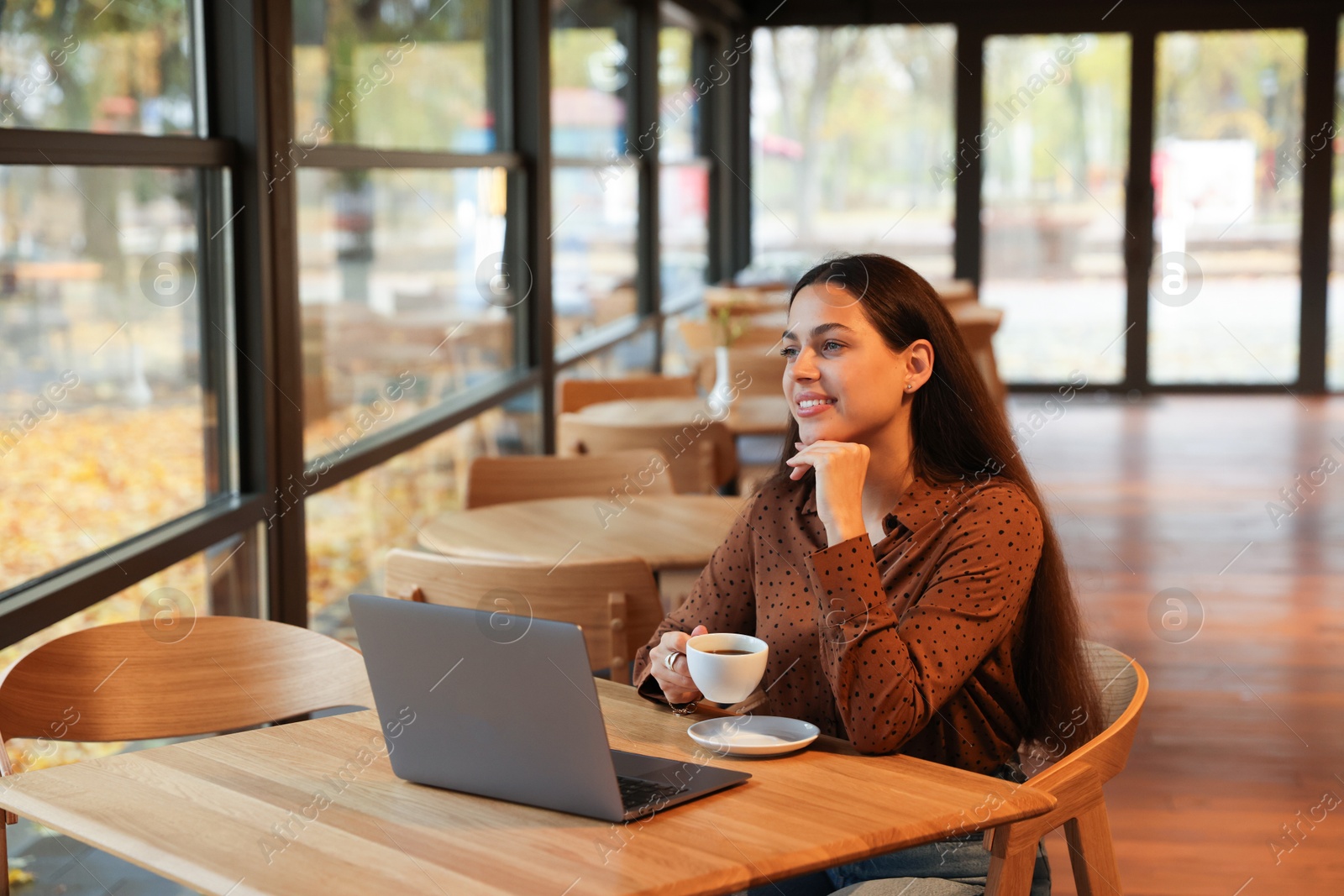 Photo of Woman with cup of coffee working at table in cafe