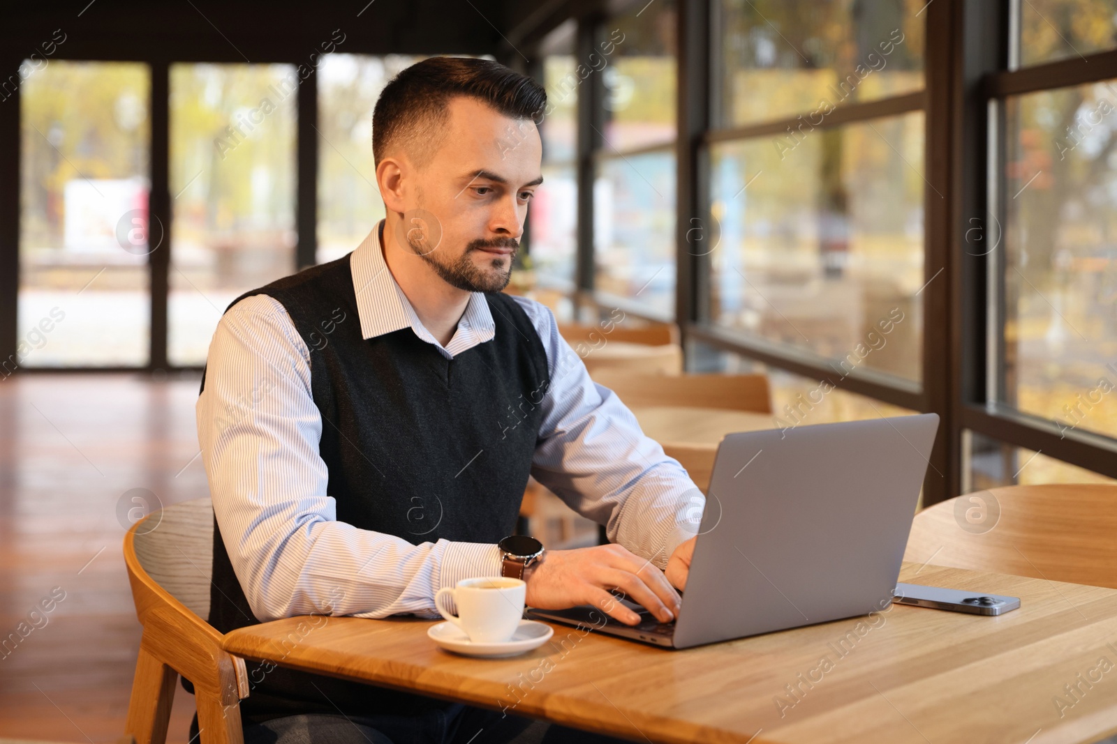 Photo of Man working on laptop at table in cafe