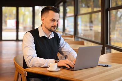 Photo of Man working on laptop at table in cafe