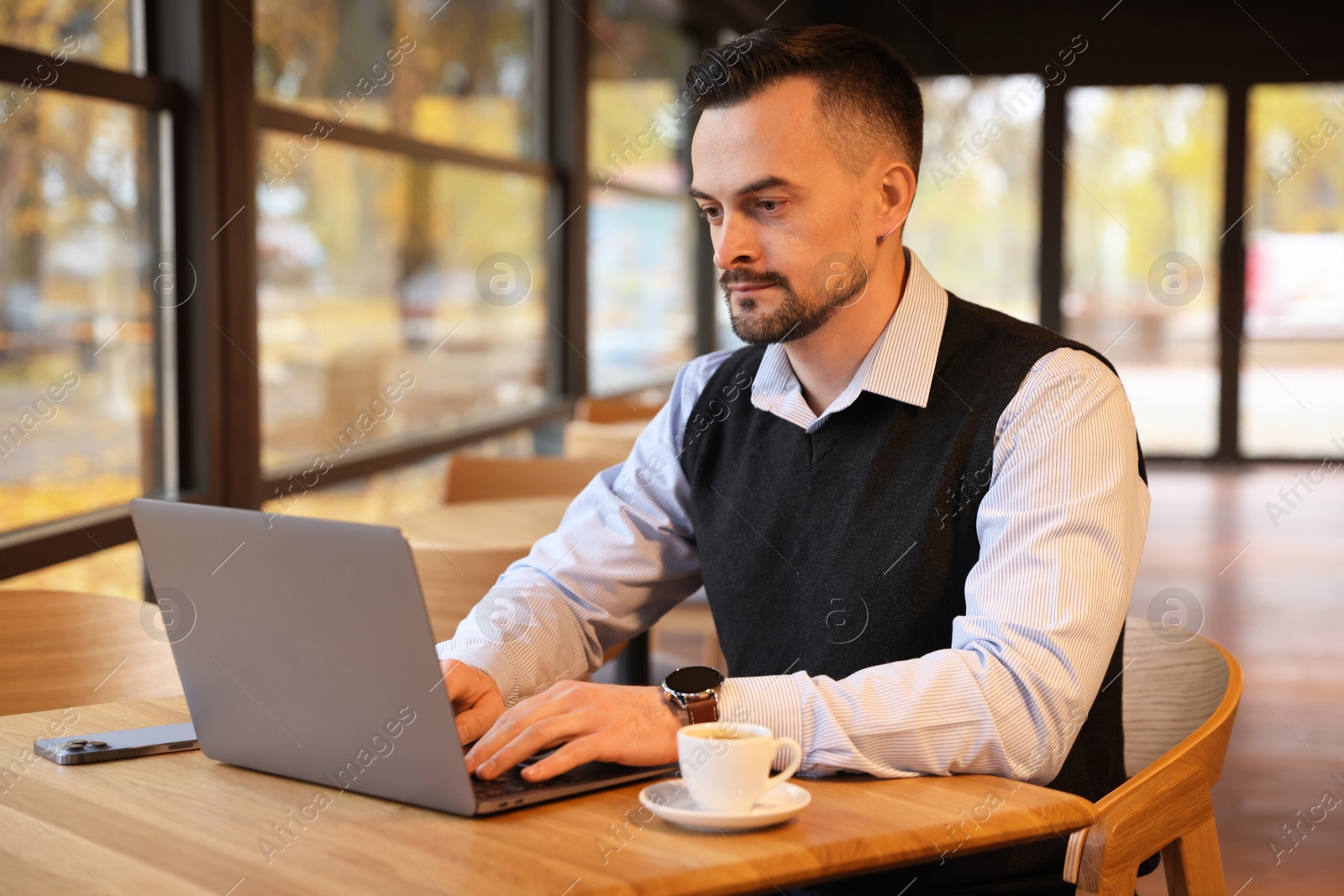 Photo of Man working on laptop at table in cafe