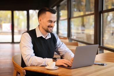 Photo of Man working on laptop at table in cafe