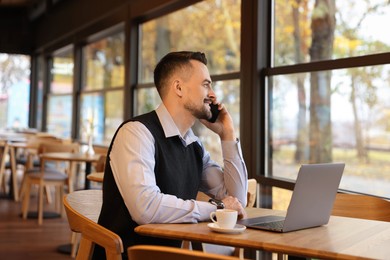 Photo of Man talking on smartphone while working at table in cafe