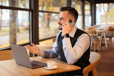 Photo of Man talking on smartphone while working at table in cafe