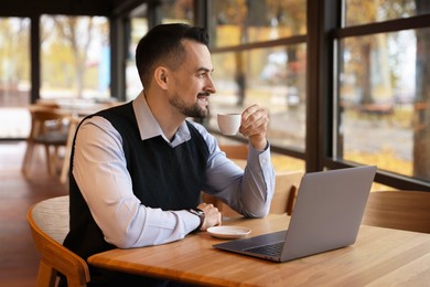 Photo of Man with cup of coffee working at table in cafe