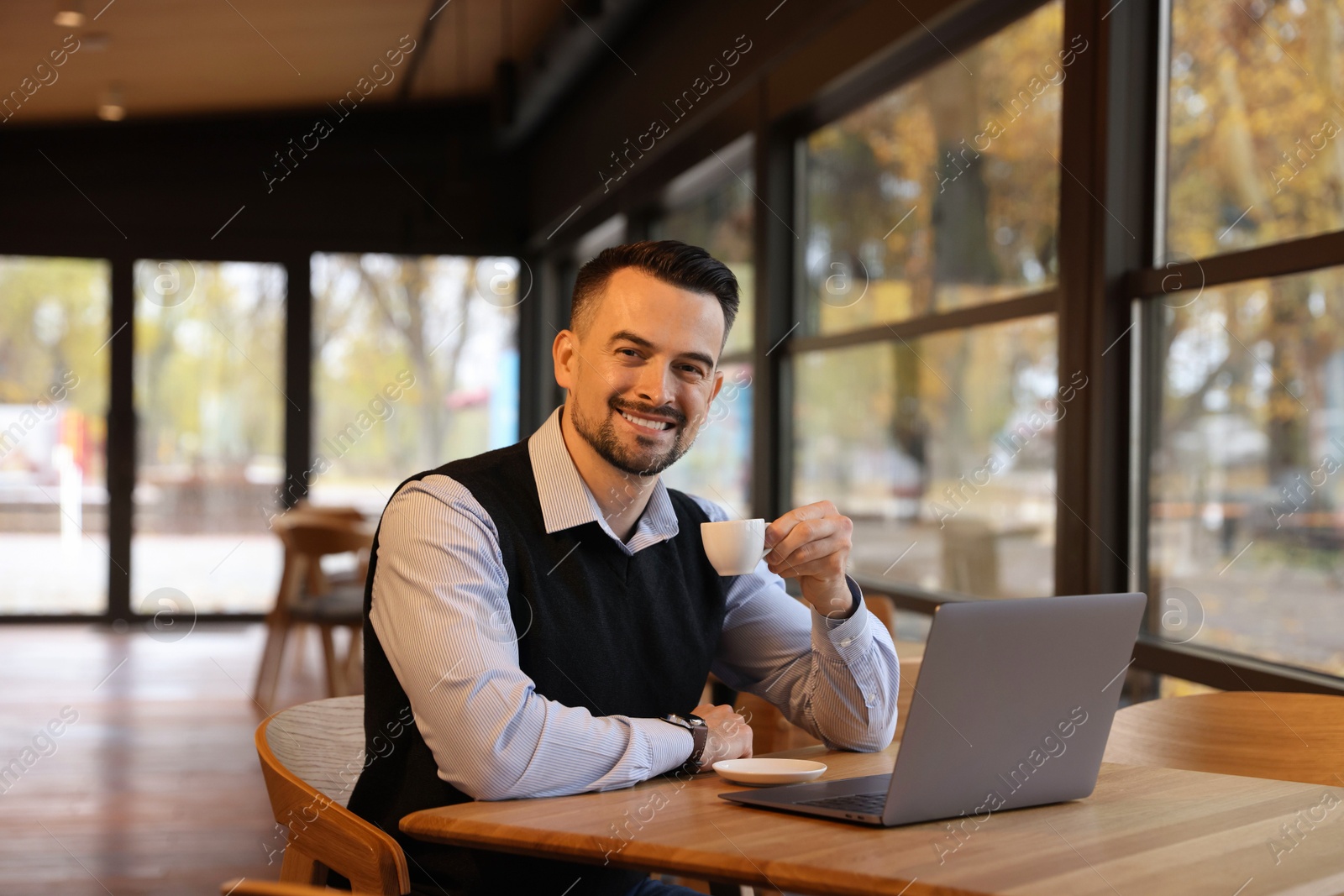 Photo of Man with cup of coffee working at table in cafe