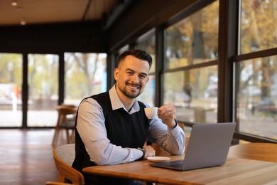 Photo of Man with cup of coffee working at table in cafe