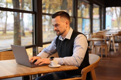 Photo of Man working on laptop at table in cafe