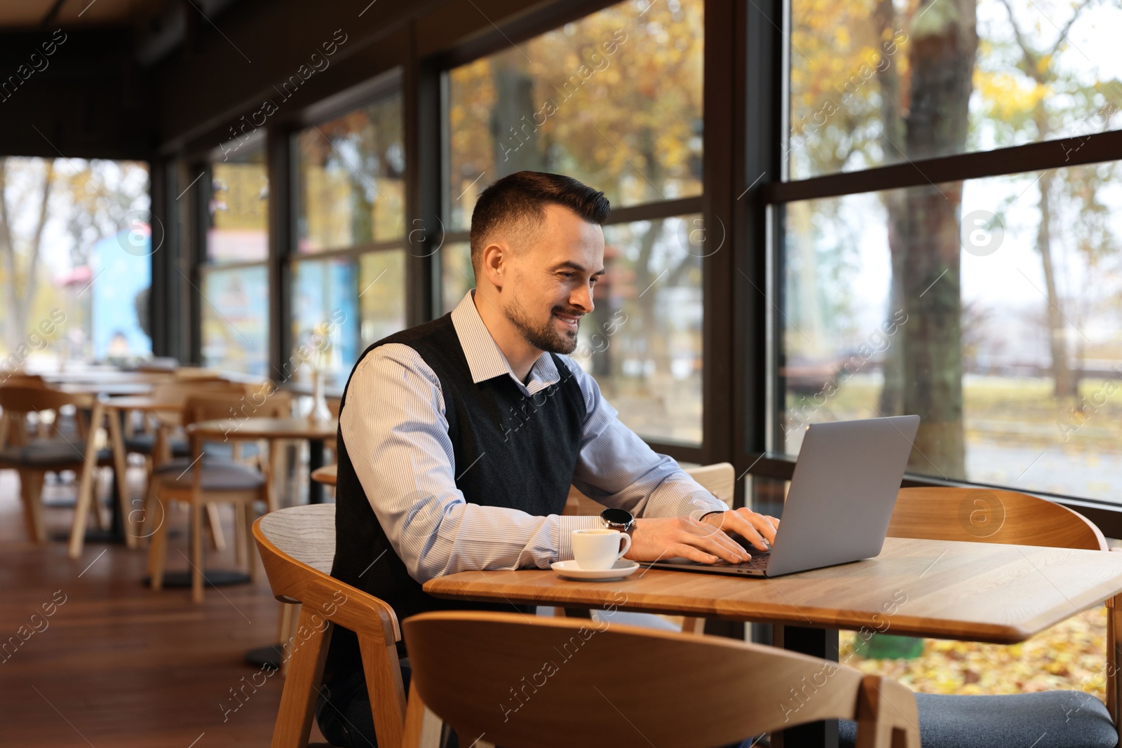 Photo of Man working on laptop at table in cafe