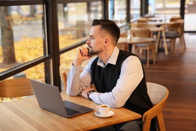 Photo of Man with laptop and cup of coffee at table in cafe