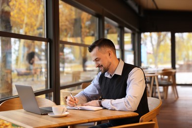 Photo of Man taking notes at table in cafe