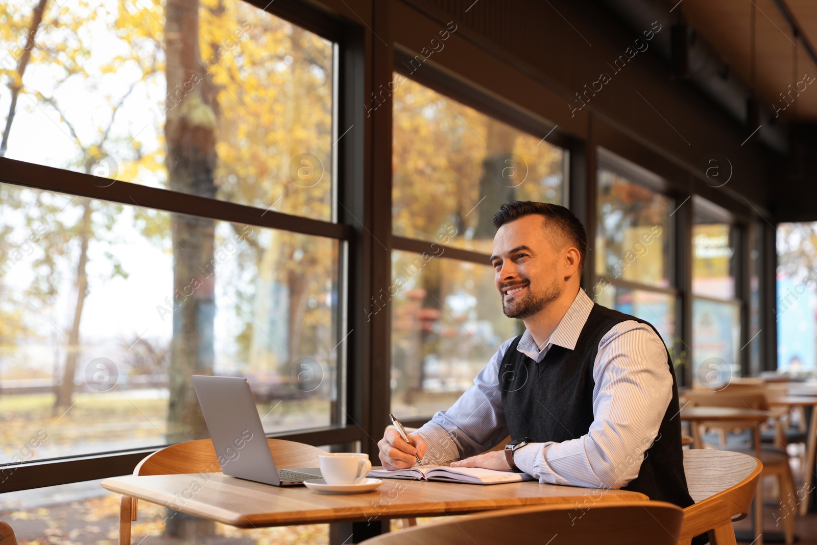 Photo of Man taking notes at table in cafe