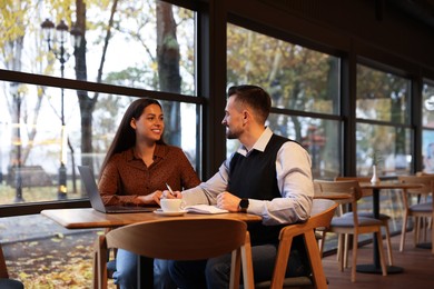 Photo of Colleagues with laptop working together in cafe