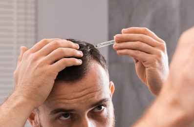 Baldness problem. Man applying serum onto hairline near mirror in bathroom, closeup