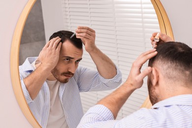 Baldness problem. Man applying serum onto hairline near mirror in bathroom