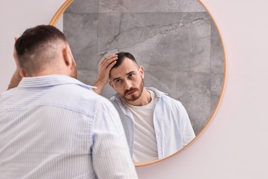 Baldness problem. Man with receding hairline near mirror in bathroom