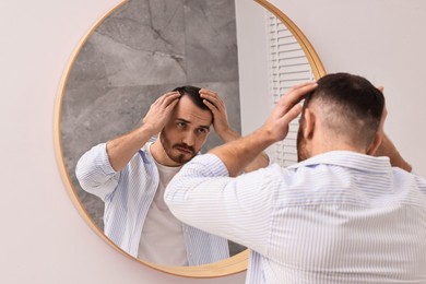 Photo of Baldness problem. Man with receding hairline near mirror in bathroom