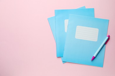 Photo of Copybooks and pen on pink background, flat lay. School stationery