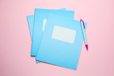 Photo of Copybooks and pen on pink background, flat lay. School stationery