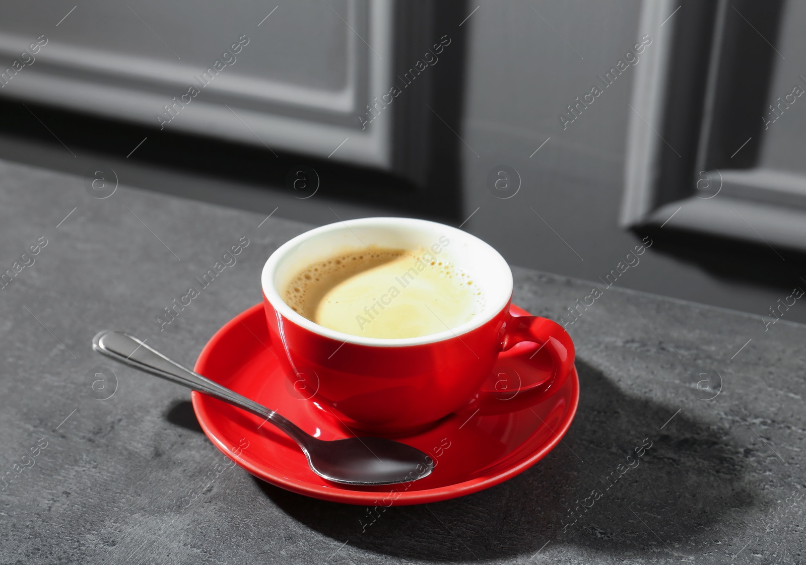 Red cup of aromatic coffee, saucer and spoon on dark textured table Photo of Red cup of aromatic coffee, saucer and spoon on dark textured table