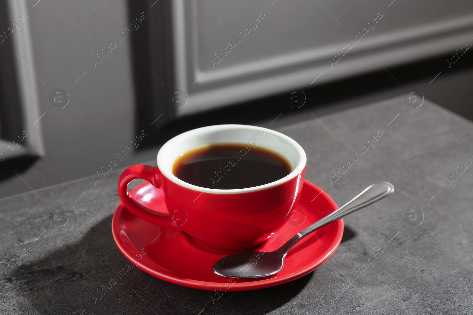 Red cup of aromatic coffee, saucer and spoon on dark textured table, closeup Photo of Red cup of aromatic coffee, saucer and spoon on dark textured table, closeup
