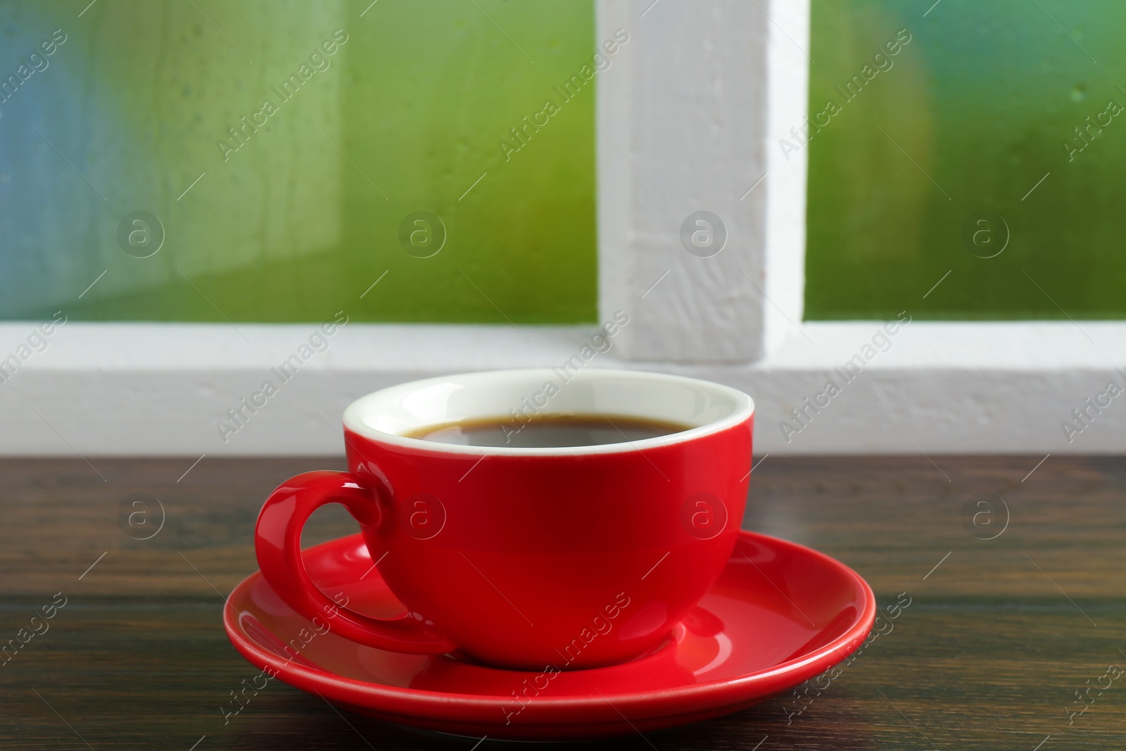 Red cup of aromatic coffee and saucer on wooden sill near window, closeup Photo of Red cup of aromatic coffee and saucer on wooden sill near window, closeup