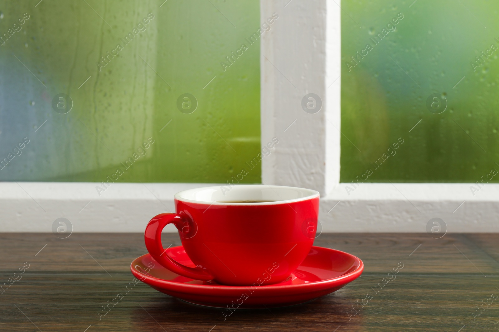 Red cup of aromatic coffee and saucer on wooden sill near window, closeup Photo of Red cup of aromatic coffee and saucer on wooden sill near window, closeup