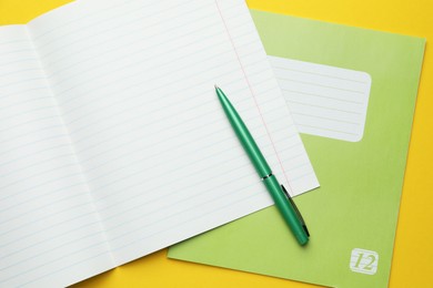 Photo of Copybooks and pen on yellow background, top view