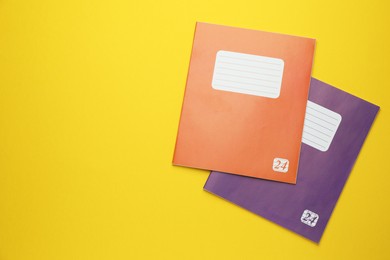 Photo of Orange and purple copybooks on yellow background, flat lay. Space for text