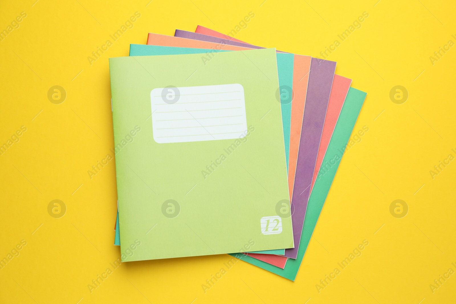 Photo of Colorful copybooks on yellow background, top view