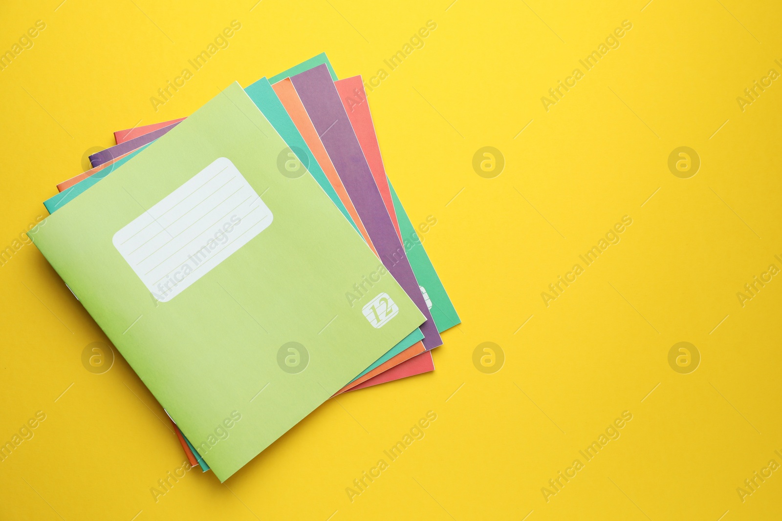 Photo of Colorful copybooks on yellow background, top view. Space for text