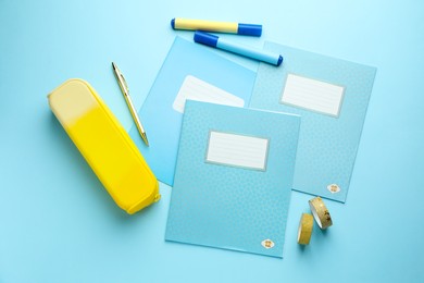 Photo of Copybooks and other school stationery on light blue background, flat lay