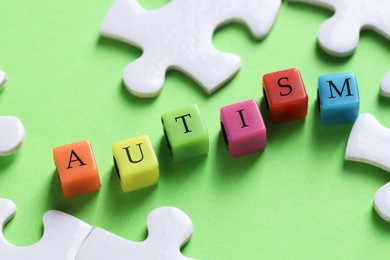 Photo of Word Autism made with colorful cubes and puzzle pieces on green background, closeup