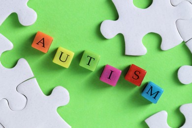 Photo of Word Autism made with colorful cubes and puzzle pieces on green background, flat lay